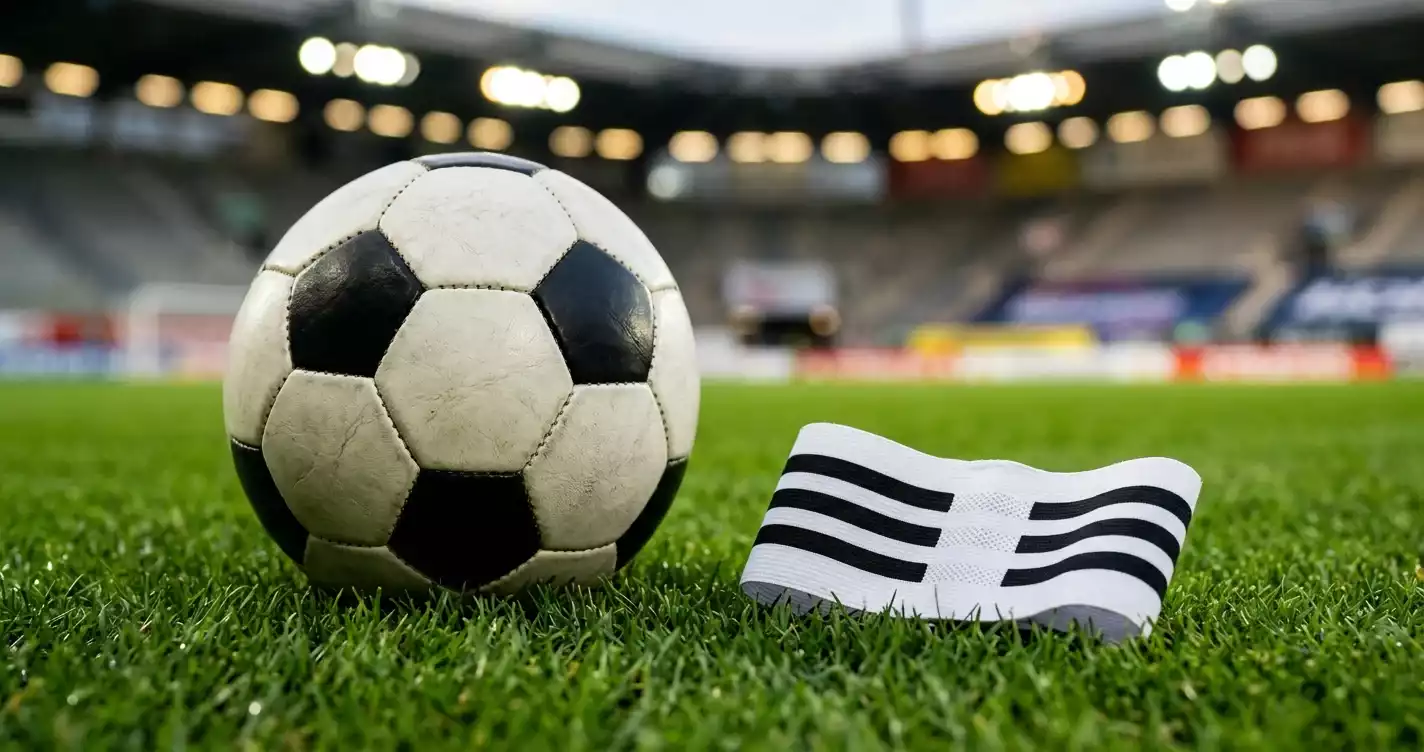 Nærbilde av en fotball og et kapteinsbind på gresset før avspark